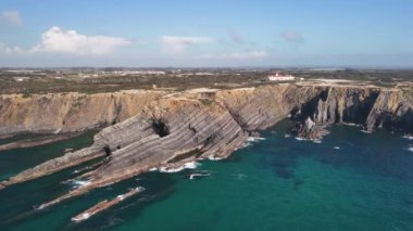 Deniz feneri Farol do Cabo Sardao Portekiz 'deki dik kayanın kenarında. Uçan kaya oluşumunun katmanları aşağıda.