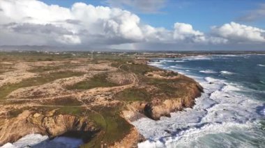 Alentejo bölgesinin batısındaki Portekiz kıyı şeridinin havadan görüntüsü. Ön planda dev okyanus sörfü ve arka planda dramatik bulutlar ve gökkuşağı.