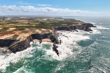 Uzaktaki kayalık okyanus kıyısı ve deniz feneri Cabo Sardao 'nun kuş bakışı görüntüsü. Dik kayalıklar ve altında fırtınalı okyanus. Portekiz