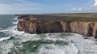 İnsansız hava aracı devasa sahil kayalıklarının ve dev okyanus dalgalarının üzerinden yükseliyor. Alentejo bölgesi, Portekiz 