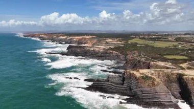 İnsansız hava aracı okyanus kıyısında dev uçurumlar ve kırılan dalgalarla yükselir. Alentejo kırsalında Trilho dos Pescadores, Portekiz