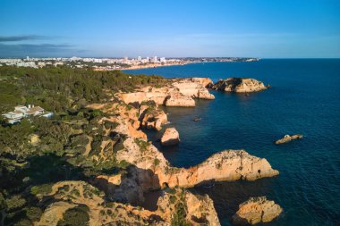 Ön plandaki kireçtaşı uçurumlarının panoramik manzarası ve arka plandaki Portimao şehri. Algarve, Portekiz