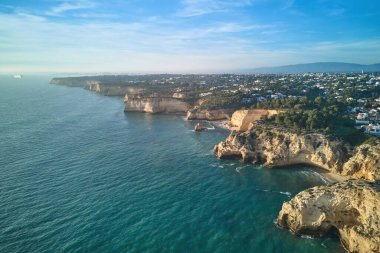 Sıcak altın ışıkta uzaktaki kayalık kıyı şeridinin çarpıcı hava manzarası. Portekiz 'deki Algarve bölgesinin sakin ve huzurlu manzarası