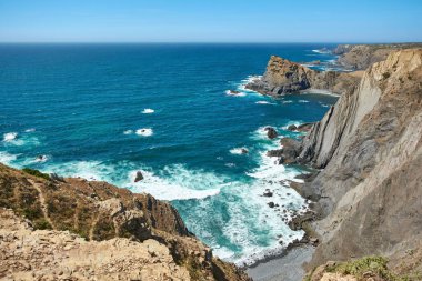 Stunning coastal view of steep cliffs meeting stormy Atlantic Ocean with crashing waves in Arrifana, Portugal clipart