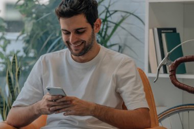 Evdeki kanepede cep telefonlu genç adam.