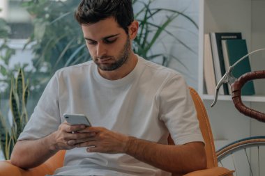 Evdeki kanepede cep telefonlu genç adam.