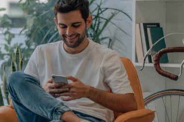 Evdeki kanepede cep telefonlu genç adam.