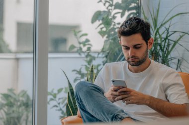 Genç adam cep telefonuyla evde.