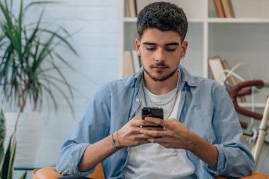 Evdeki genç adam cep telefonuna bakıyor.