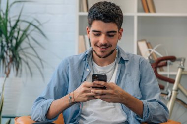 Evdeki genç adam cep telefonuna bakıyor.