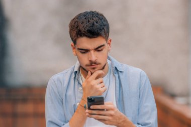 Genç adam şüpheli bir şekilde cep telefonuna bakıyor.
