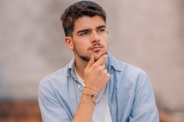 Çekici, genç, sakallı, beyaz bir adam sokakta, düşünceli bir ifadeyle.