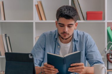 Öğrenci evde ders çalışıyor ya da masada dizüstü bilgisayarla kitap okuyor.