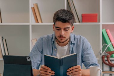 Öğrenci evde ders çalışıyor ya da masada dizüstü bilgisayarla kitap okuyor.
