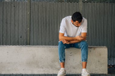 Sokaktaki genç adam cep telefonuyla oturuyor.