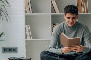 young man reading textbook at home or library