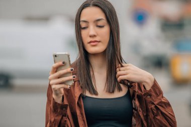 Sonbaharda sokakta cep telefonuna bakan bir kız.