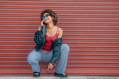 Kentsel modern kız kırmızı arka planda cep telefonuyla konuşuyor.