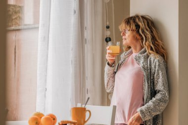 Evde meyve suyu içen orta yaşlı bir kadın.