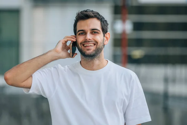 Portret Młodego Mężczyzny Ulicy Uśmiechniętego Telefonem Komórkowym — Zdjęcie stockowe