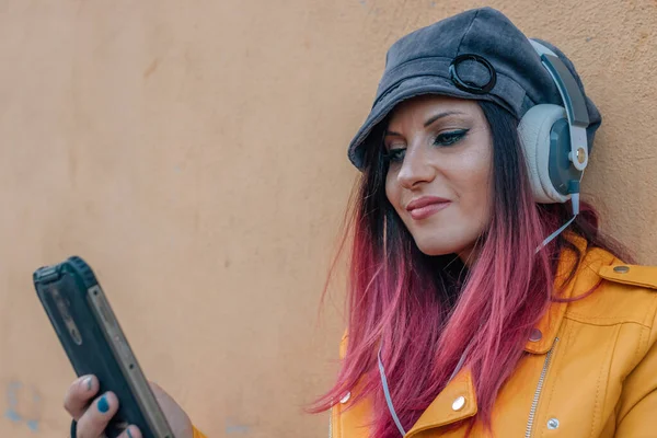woman with dyed red hair with headphones and mobile phone outdoors