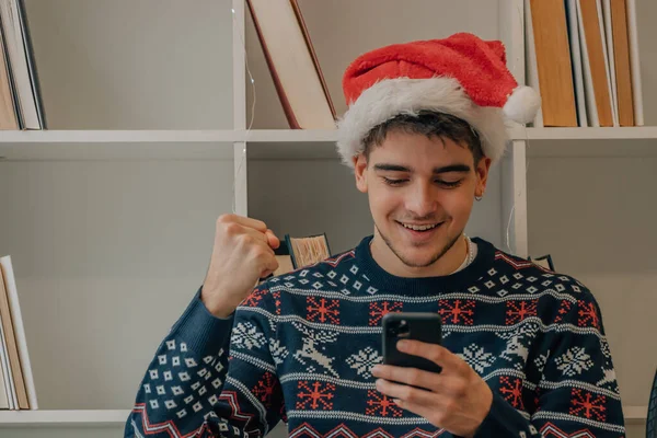 Boldog Fiatalember Otthon Mobiltelefon Mikulás Kalap Karácsonykor — Stock Fotó