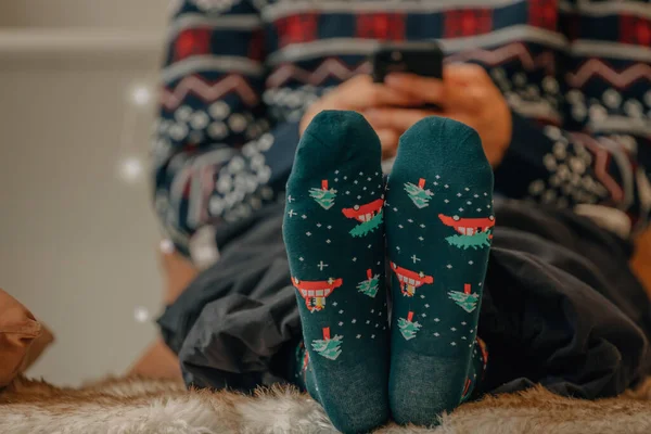 feet with christmas socks of young man at home with mobile phone