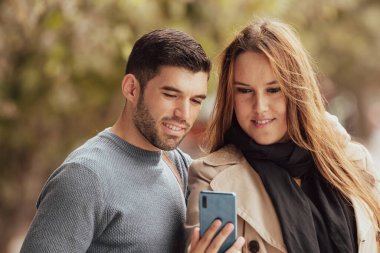 Sonbaharda çiftler sokakta cep telefonlarına bakarlar.