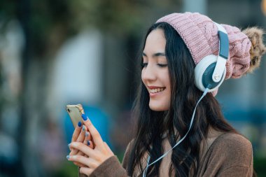 Kışın sokakta şapkalı, cep telefonu ve kulaklıklı bir kız.