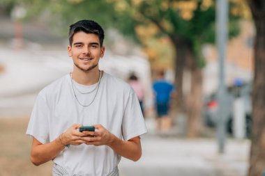 Sokakta cep telefonu ya da akıllı telefonuyla gülümseyen genç adamın portresi.