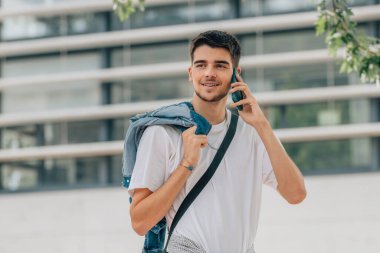 Genç adam sokakta yürüyor cep telefonu ya da cep telefonuyla konuşuyor.