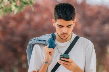 Genç adam caddede cep telefonuna bakıyor.