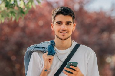 Genç adam caddede cep telefonuna bakıyor.