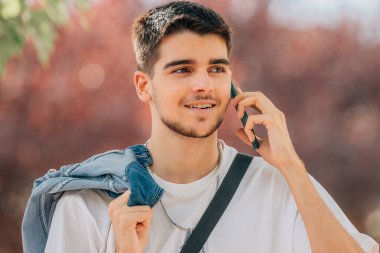 Genç adam sokakta cep telefonuyla konuşuyor.