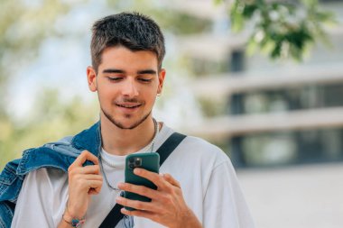 Sokaktaki genç adam cep veya cep telefonuna bakıyor.