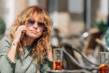 Barın terasında cep telefonuyla konuşan orta yaşlı bir kadın.