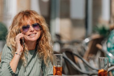 Barın terasında cep telefonuyla konuşan orta yaşlı bir kadın.