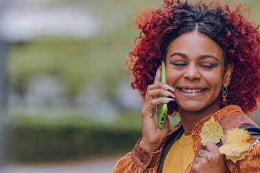 Cep telefonlu ve sonbahar yapraklı siyah Latin Amerikalı