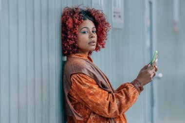 Sokak duvarında cep telefonu olan Afro-Amerikan Latin kadın.