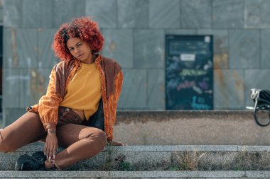 Afrikalı Amerikalı hippi kadın sokakta oturmuş kameraya bakıyor.