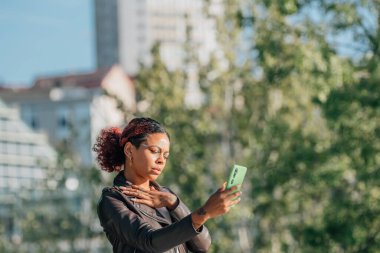 Siyah Latin Amerikalı kız dışarıda fotoğraf çekiyor ya da kayıt yapıyor.