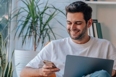 Adam evde dizüstü bilgisayar ve cep telefonuyla çalışıyor.