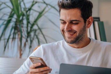Adam evde dizüstü bilgisayar ve cep telefonuyla çalışıyor.