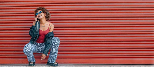 stock image young black woman with mobile phone in the street with red background