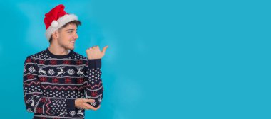 isolated young man in christmas clothes and santa claus hat on blue background