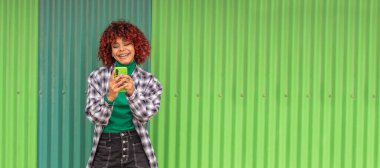 girl with mobile phone in the street with green wall in the background