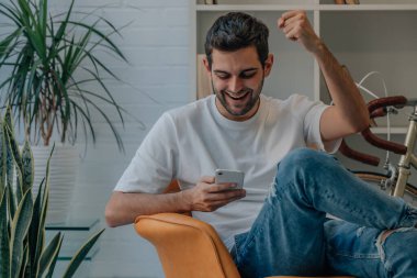 Evdeki genç adam cep telefonuna bakarak mutluluktan uçuyor.