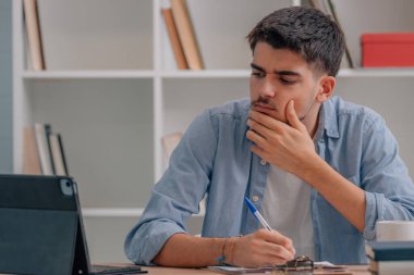young man or student at desk with laptop thinking with doubt or deciding