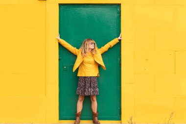 Sarı duvarlı yeşil kapıda orta yaşlı mutlu bir kadın