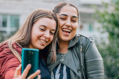 smiling friends on the street with mobile phone